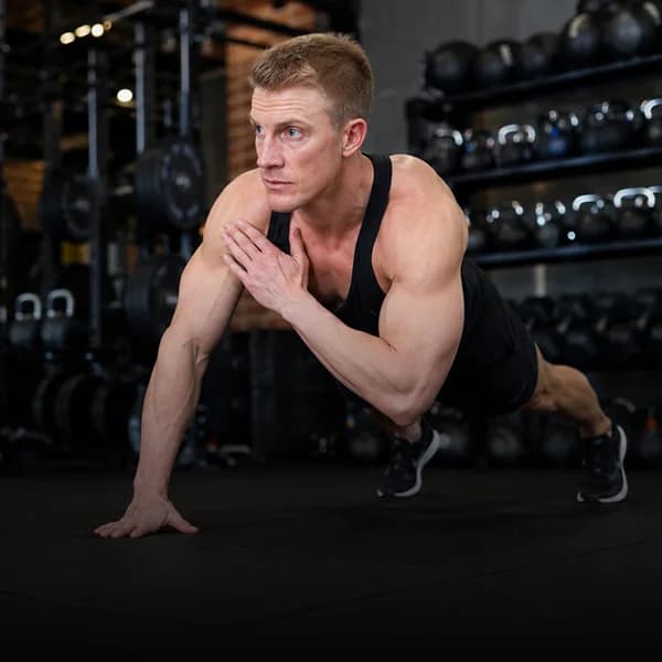 A man holding a one-armed press-up position on the floor of a dimly lit gym.